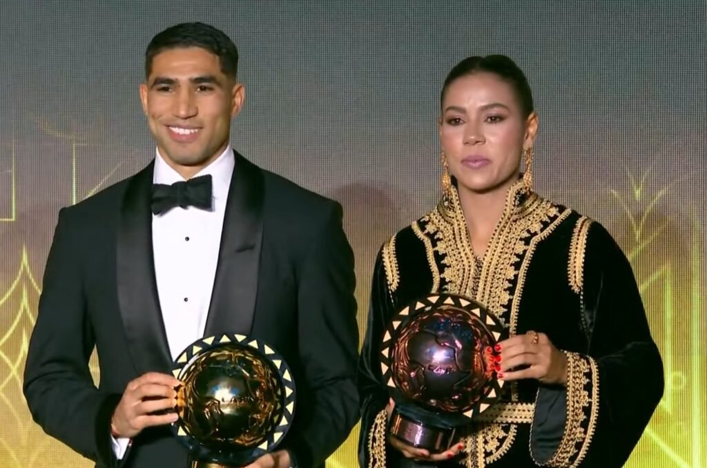 Achraf Hakimi and Ghizlane Chebbak holding their CAF African Player of the Year and African Women’s Player of the Year trophies at the CAF Awards ceremony for Morocco.